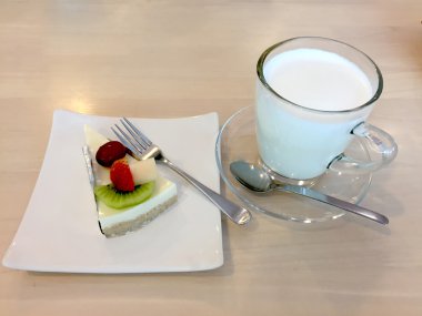 Dilim Cheesecake tatlı çatal ve süt ile çilek, kivi, grafiği ve ahşap masa üzerinde tabakta kavun Komposto ile tepesinde 