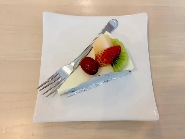 Tranche de gâteau au fromage garnie de compote de fraise, kiwi, grappin et cantaloup sur une assiette sur une table en bois avec fourchette à dessert — Photo