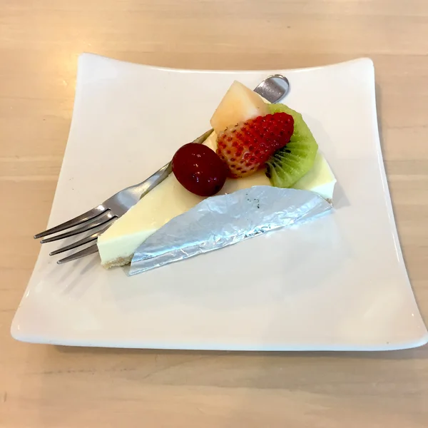 Bit av Cheesecake toppad med jordgubbar, Kiwi, Grap och cantaloupemelon kompott på plattan på trä bord med Dessert gaffel — Stockfoto