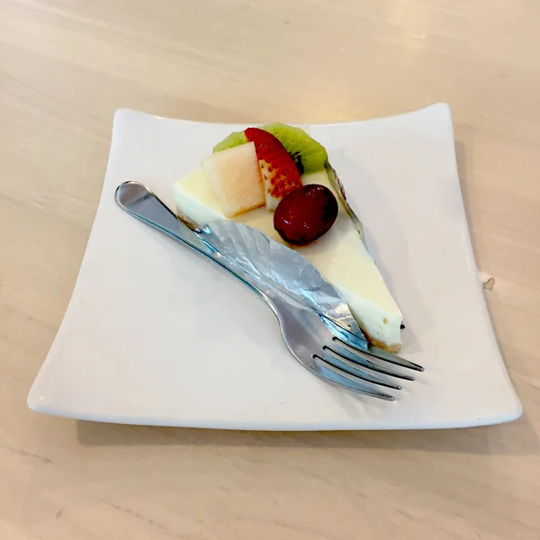 Tranche de gâteau au fromage garnie de compote de fraise, kiwi, grappin et cantaloup sur une assiette sur une table en bois avec fourchette à dessert — Photo