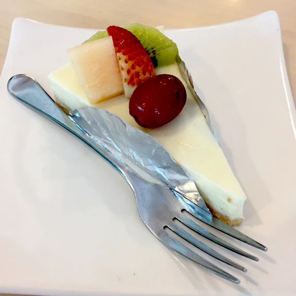 Bit av Cheesecake toppad med jordgubbar, Kiwi, Grap och cantaloupemelon kompott på plattan på trä bord med Dessert gaffel — Stockfoto
