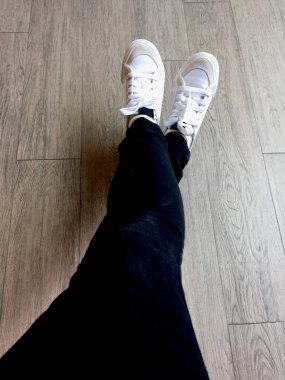 Spor ayakkabı beyaz ve kot kız bacaklar ahşap arka plan üzerinde siyah 