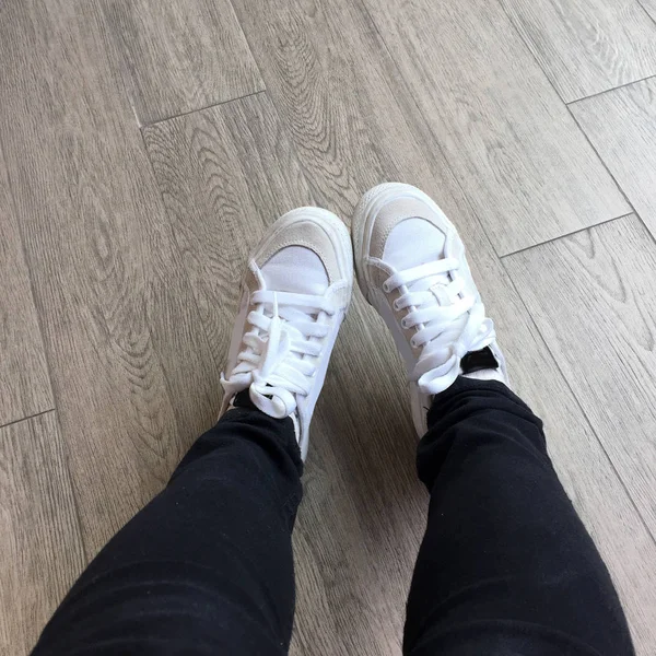 Λευκά Sneakers και μαύρο τζιν κορίτσι πόδια σε ξύλο φόντο — Φωτογραφία Αρχείου