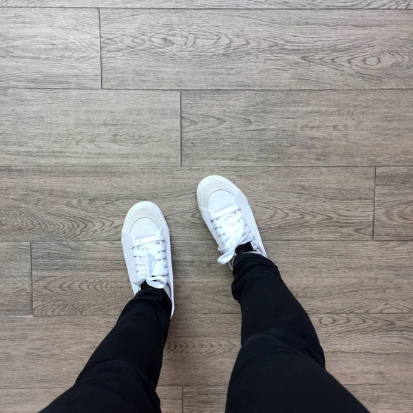 Weiße Turnschuhe und schwarze Jeans auf Mädchenbeinen auf Holzhintergrund — Stockfoto