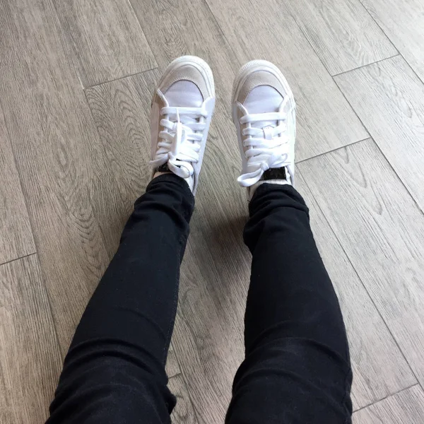 Witte Sneakers en zwarte Jeans op meisje benen op houten achtergrond — Stockfoto