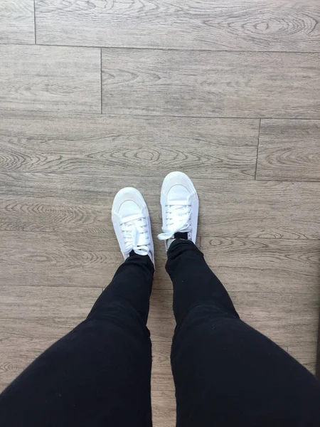 Witte Sneakers en zwarte Jeans op meisje benen op houten achtergrond — Stockfoto