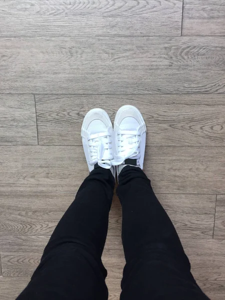 Witte Sneakers en zwarte Jeans op meisje benen op houten achtergrond — Stockfoto