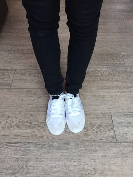 Vita Sneakers och svart Jeans på flicka ben på trä bakgrund — Stockfoto