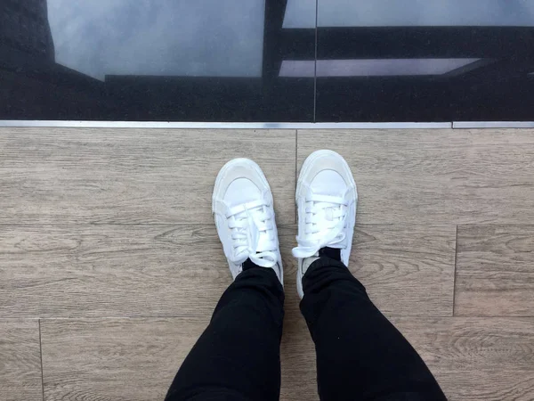 Baskets blanches et jeans noirs sur les jambes de fille sur fond en bois — Photo