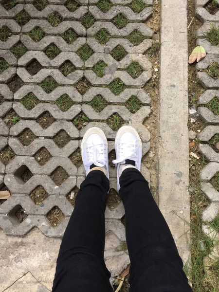 Weiße Turnschuhe und schwarze Jeans auf Mädchenbeinen auf Holzhintergrund — Stockfoto