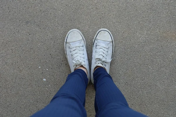 Молодая женщина в синих джинсах и белых кроссовках на улицах — стоковое фото