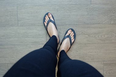 Genç kız bacaklarını ahşap zemin üzerinde siyah Flipflop Sandaletler içinde 