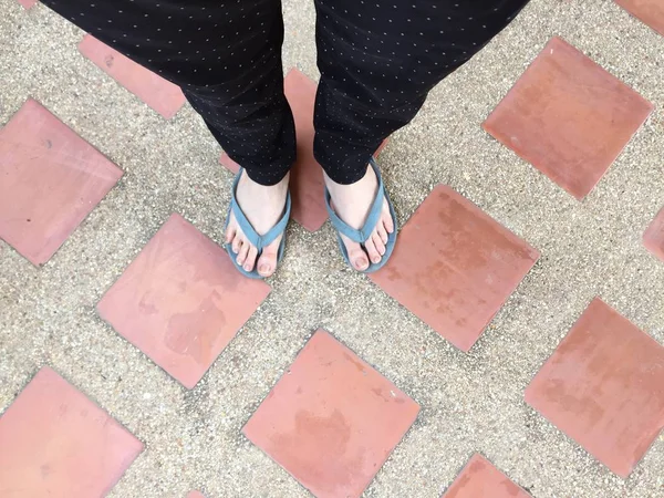 Piernas femeninas en sandalias sobre fondo de baldosa —  Fotos de Stock
