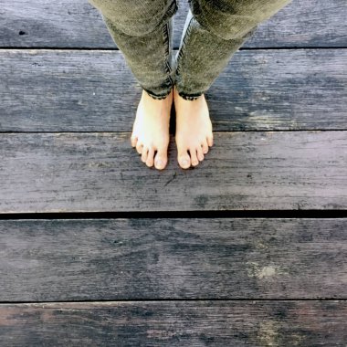 Kadının kot pantolon ve ahşap arka plan üzerinde çıplak ayak 