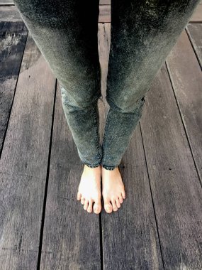 Kadının kot pantolon ve ahşap arka plan üzerinde çıplak ayak 