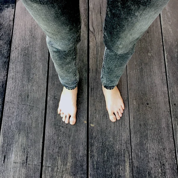 Ženy džíny a bosé nohy na dřevěné pozadí — Stock fotografie