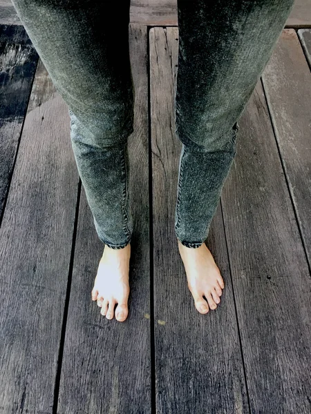 Kadının kot pantolon ve ahşap arka plan üzerinde çıplak ayak 
