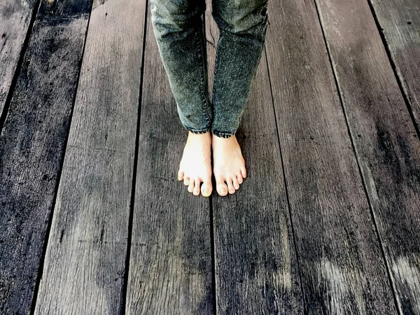Женские джинсы и голые ноги на деревянном фоне — стоковое фото