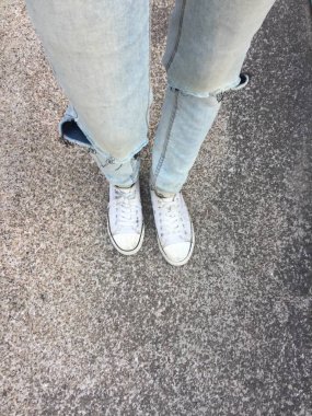 Kadının bacakları mavi kot pantolon ve zemin üzerinde beyaz spor ayakkabı 