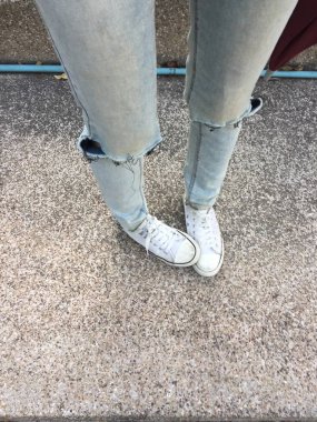 Kadının bacakları mavi kot pantolon ve zemin üzerinde beyaz spor ayakkabı 