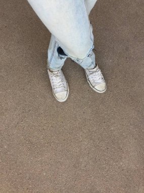 Kadının bacakları mavi kot pantolon ve zemin üzerinde beyaz spor ayakkabı 