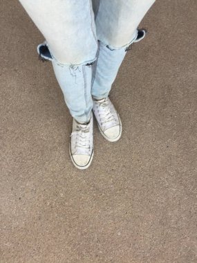 Kadının bacakları mavi kot pantolon ve zemin üzerinde beyaz spor ayakkabı 