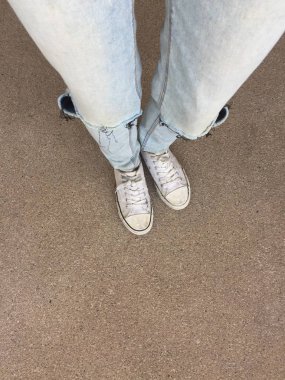 Kadının bacakları mavi kot pantolon ve zemin üzerinde beyaz spor ayakkabı 