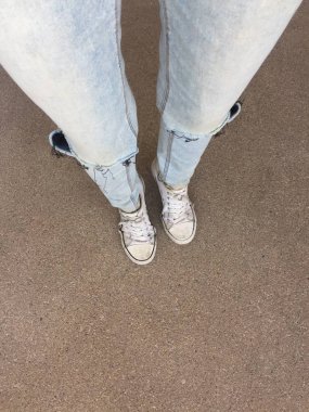 Kadının bacakları mavi kot pantolon ve zemin üzerinde beyaz spor ayakkabı 