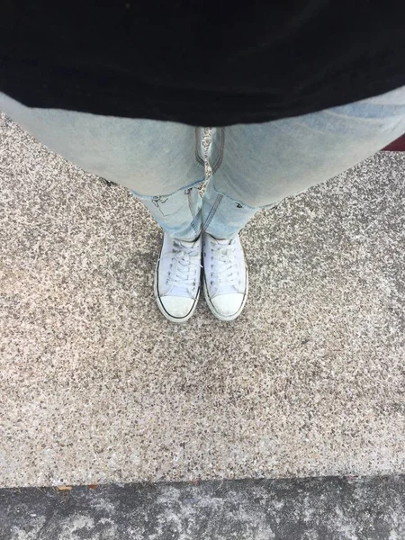 Jambes de femme en jeans bleus et baskets blanches sur le sol — Photo