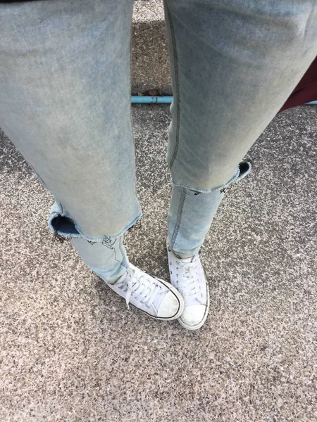 Piernas de mujer en pantalones vaqueros azules y zapatillas blancas en el piso —  Fotos de Stock