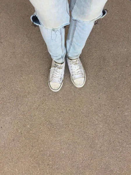 Kvinnans ben i blå Jeans och vita Sneakers på golvet — Stockfoto