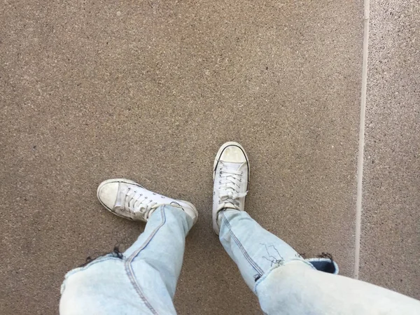 Pernas de mulher em calças de ganga azuis e tênis brancos no chão — Fotografia de Stock
