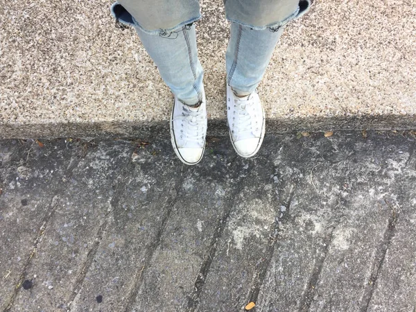 Jambes de femme en jeans bleus et baskets blanches sur le sol — Photo
