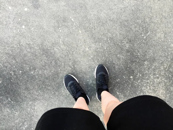 Pieds féminins en Sneakers noires sur fond de sol — Photo