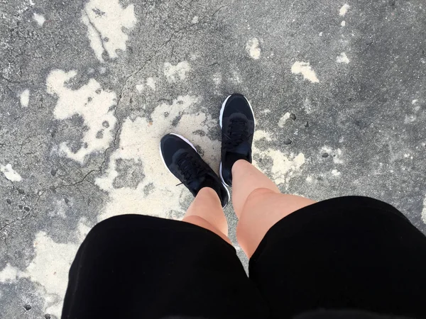Vrouwelijke voeten in zwarte sneakers op vloer achtergrond — Stockfoto