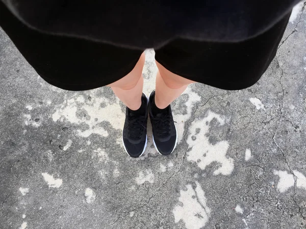 Frauenfüße in schwarzen Turnschuhen auf Bodengrund — Stockfoto