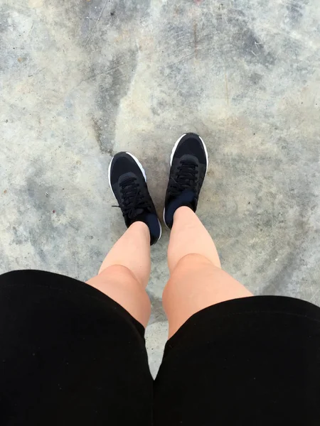 Frauenfüße in schwarzen Turnschuhen auf Bodengrund — Stockfoto