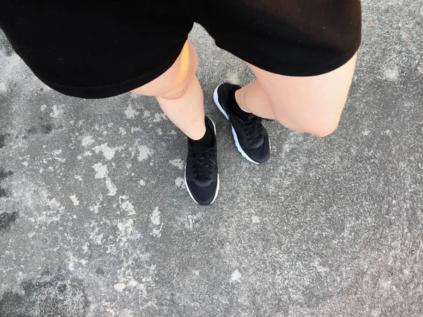 Pieds féminins en Sneakers noires sur fond de sol — Photo