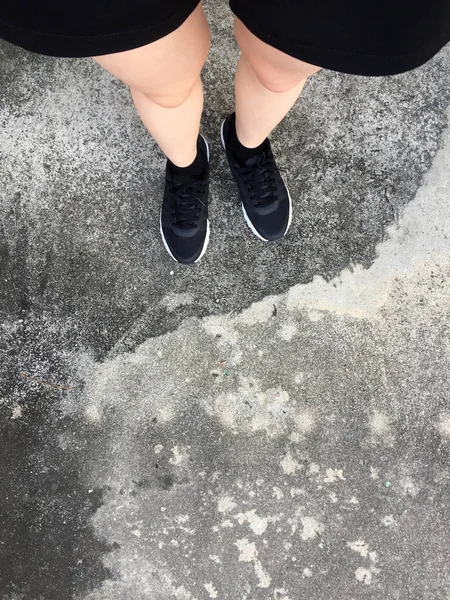 Piedi femminili in scarpe da ginnastica nere su fondo pavimento — Foto Stock