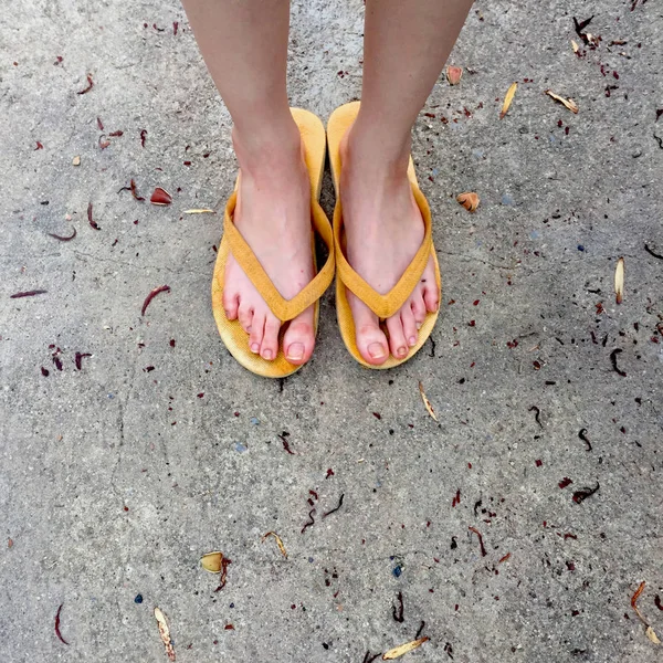 Sandálias amarelas nos pés femininos no fundo do solo — Fotografia de Stock
