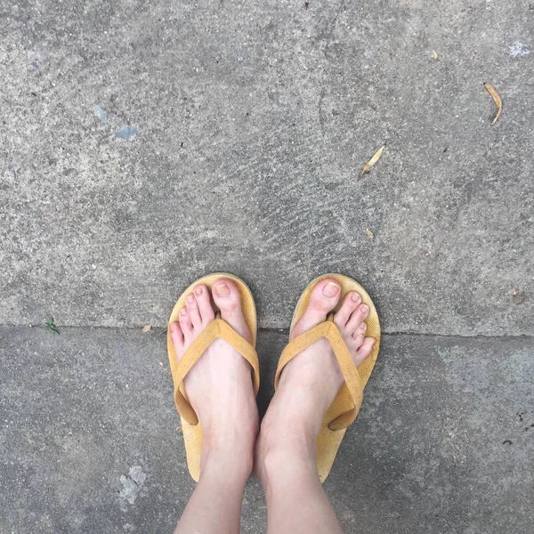 Gula sandaler på kvinnliga fötter på marken bakgrund — Stockfoto