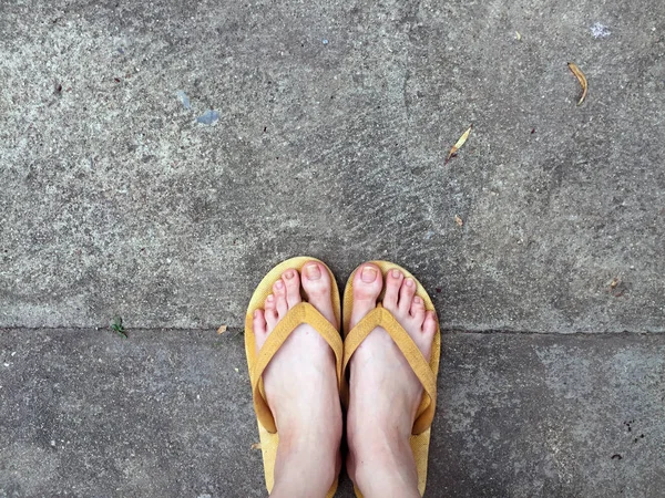 地面背景上女性脚上的黄色凉鞋 — 图库照片