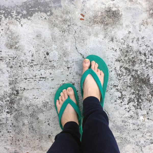 Pés de uma mulher vestindo sandálias verdes no chão de concreto velho — Fotografia de Stock