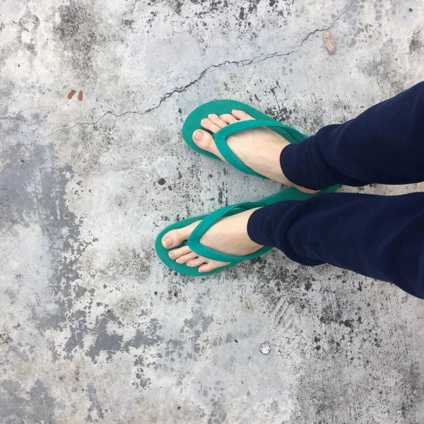 Pés de uma mulher vestindo sandálias verdes no chão de concreto velho — Fotografia de Stock