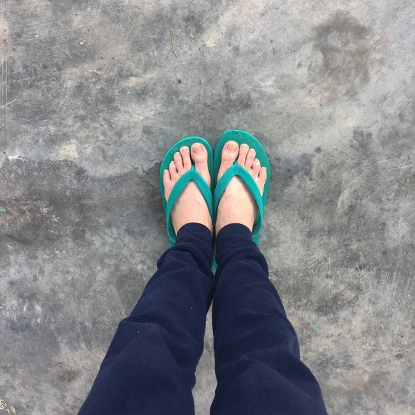 Fötter av en kvinna som bär gröna sandaler på gamla betonggolvet — Stockfoto