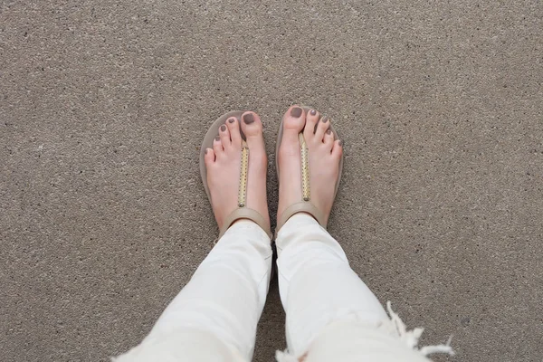 Selfie pés vestindo sandálias de ouro e calça branca no chão — Fotografia de Stock