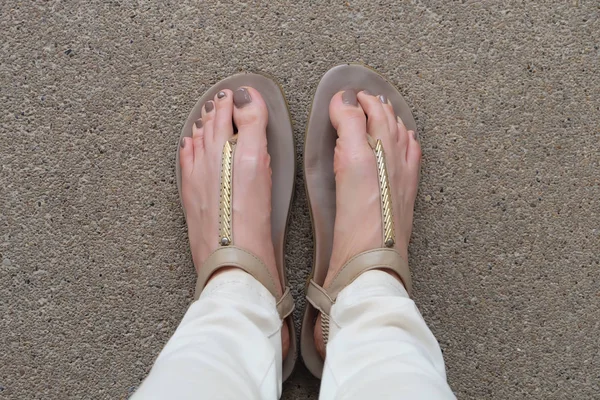 Selfie Feet Wearing Gold Sandals and White Jeans on Ground