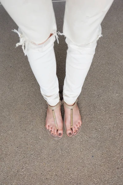 Selfie Feet portant des sandales en or et un jean blanc sur fond de sol — Photo