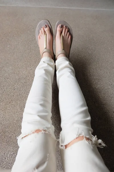 Selfie Goldsandalen und weiße Jeans auf weiblichen Füßen auf dem Boden Hintergrund. — Stockfoto