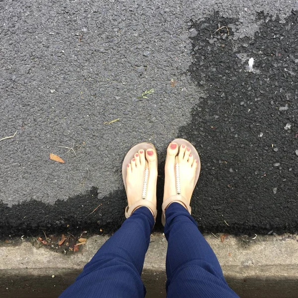 Pies de cerca con clavo marrón en sandalias de oro y pantalones azules en los pies femeninos en el fondo del suelo —  Fotos de Stock
